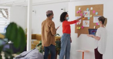 Çok ırklı kadın ve erkek iş adamlarından oluşan bir grup modern ofiste yüz maskeleri takarak, ağır çekimde beyin fırtınası yapıyorlar. Coronavirus Covid 19 salgını sırasında işyerinde sağlık ve hijyen.