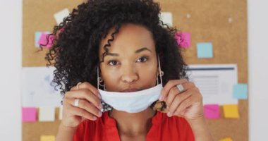 Ofiste durmuş, ağır çekimde maskesini takan melez kadın iş kadınlarının portresi. Coronavirus Covid 19 salgını sırasında işyerinde sağlık ve hijyen.