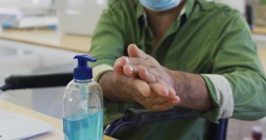 Yüz maskesi takmış melez bir adamın, ofiste maskesinde oturup el dezenfektanı ile el dezenfekte etmesi, ağır çekimde. Coronavirus Covid 19 salgını sırasında işyerinde sağlık ve hijyen.
