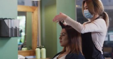 Kafkas kadın kuaför yüz maskesi takarak kuaförde çalışıyor, Kafkas kadın saçlarına bigudi takıyor, ağır çekimde. Coronavirus Covid 19 salgını sırasında işyerinde sağlık ve hijyen.