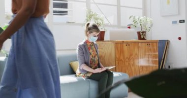 Beyaz kadın ve melez erkek iş arkadaşı yüz maskesi takıyor, mesafeli, dirseklerine dokunarak selamlıyor, ağır çekimde. Coronavirus Covid 19 salgını sırasında işyerinde sağlık ve hijyen.