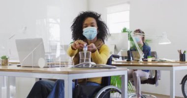 Yarış masasında oturan melez kadın koruyucu ekranlı, yüz maskeli, ellerini santimerle dezenfekte eden, ağır çekimde. Coronavirus Covid 19 salgını sırasında işyerinde sağlık ve hijyen.