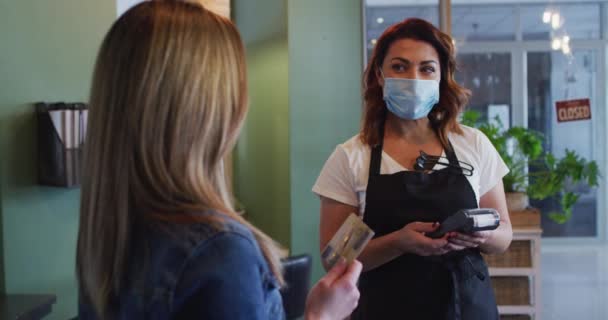 フェイスマスクを着用したヘアサロンで働く白人女性の美容師は フェイスマスクで顧客からの支払いを受け スローモーション コロナウイルスの職場での健康と衛生 Covid 19パンデミック — ストック動画