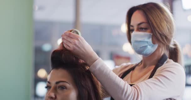 在美发厅工作的白人女性美发师戴着面罩 在白人女性的头发上放发筒 动作缓慢 Coronavirus Covid 19大流行病期间工作场所的健康和卫生 — 图库视频影像