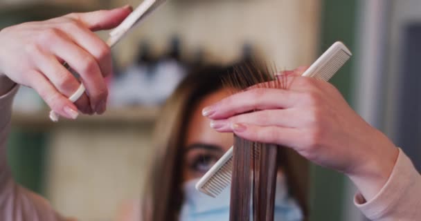 顔のマスクを身に着けているヘアサロンで働く白人女性の美容師 女性白人の顧客の髪 スローモーション コロナウイルスの職場での健康と衛生 Covid 19パンデミック — ストック動画