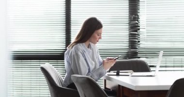 Çizgili tişörtlü beyaz bir iş kadını telefonunda sesli mesaj kaydediyor. Ofis ortamında bir konferans masasında oturuyor, profesyonel bir hava yayıyor, yavaş çekim..