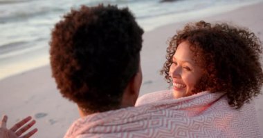 Çift ırklı çift plajda gün batımını seviyor. Kıvırcık saçlı kadın sıcak bir şekilde gülümsüyor. Okyanusla bir yakınlık anını paylaşıyorlar, dingin bir zemin olarak, yavaş çekim..