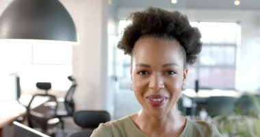 Genç bir Afro-Amerikalı kadın, bir ofis ortamında ışıl ışıl gülümsüyor. Neşeli ifadesi profesyonel çevreye hoş bir atmosfer katıyor, ağır çekimde..