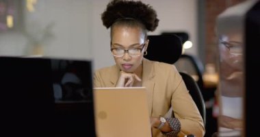 Afro-Amerikalı kadın ofisteki iş bilgisayarının ekranına dikkatle odaklanıyor. İşiyle meşgul görünüyor, verileri analiz ediyor ya da bir e-posta yazıyor, yavaş çekim..