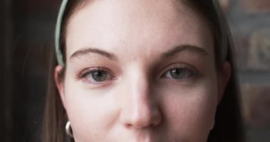 İnce bir gülüşü ve pürüzsüz bir cildi olan beyaz iş kadınının yakın çekimi. Kahverengi gözleri ve açık renk makyajı onun neşeli ifadesini tamamlıyor, ağır çekim..