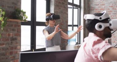 İş gezisinin bir parçası olarak VR kulaklık takan beyaz bir kadın ve Asyalı bir erkek. Sanal çevreyle etkileşime girerken elleriyle hareket ediyorlar..