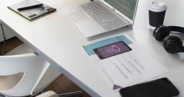 Laptop, akıllı telefon ve basılı materyaller bir iş ortamında bir masanın üzerine dizilir. Çevre, teknolojiye ve üretkenliğe, yavaş çekimde çalışmaya veya çalışmaya odaklanılmasını öneriyor..