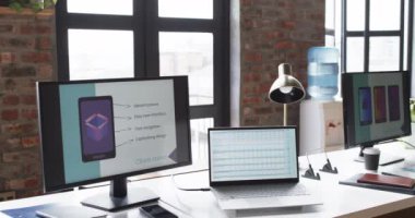 Modern ofis masası bir iş ortamında dizüstü bilgisayar, monitör ve sunum ekranı ile donatılmıştır. Dekorasyon, büyük pencerelerden gün ışığının aktığı bir tasarım stüdyosunda yaratıcı bir çalışma alanı olduğunu gösteriyor..