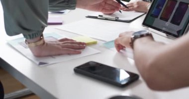 Bir grup insan iş masasında renk seçeneklerini ve tasarım planlarını tartışıyor. Elleri örnekleri işaret ediyor. Yaratıcı bir ortamda ortak bir çalışma ortamı olduğunu gösteriyor..