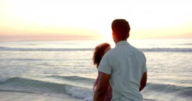 Çift ırklı çiftler, yüzleri birbirine yakın, sakin bir plaj günbatımının tadını çıkarırlar. Adam açık renk bir gömlek giyiyor, kadın desenli bir bluz giyiyor, ikisi de romantik bir anın tadını çıkarıyor, ağır çekim..