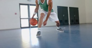 Yeşil formalı melez bir genç spor salonunda basketbol topu sürüyor. Odaklanmış ifadesi ve atletik kıyafeti yoğun bir antrenman ve ağır çekim olduğunu gösteriyor..