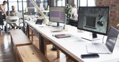 Modern ofis alanı iş için tasarlandı, birden fazla masası, bilgisayarı ve sıradan atmosferi var. Yaratıcı profesyoneller arka planda işbirliği yaparak, işbirlikçi bir çalışma ortamını vurguluyorlar.