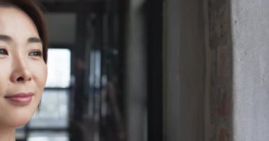 İnce makyajlı Asyalı bir iş kadını kopya alanı olan tuğla bir duvara yaslanıyor. İfadesi dalgın. Kapalı bir ortamda yavaş çekimde bir yansıma olduğunu gösteriyor..
