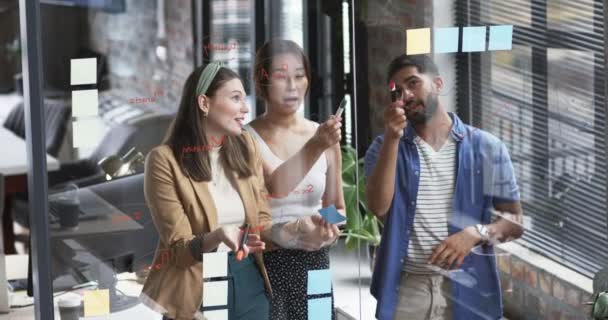 若い白人女性とアジアの同僚は ビジネスの設定でガラスの壁に粘着性のあるノートでブレインストーミングします 彼らはクリエイティブオフィスミーティングに従事し 共同ワークスペースでアイデアを共有しています — ストック動画