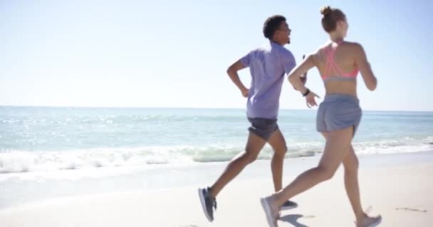 Νεαρός Σημαιοφόρος Και Λευκή Γυναίκα Κάνουν Τζόκινγκ Μια Ηλιόλουστη Παραλία — Αρχείο Βίντεο