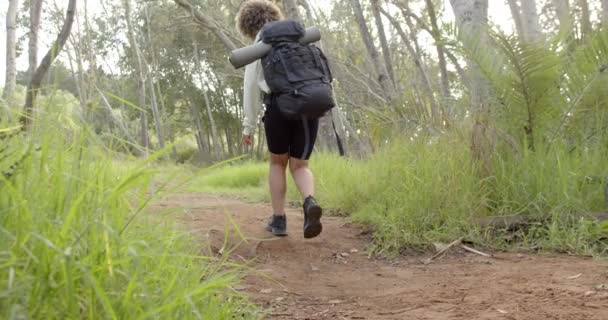 头发卷曲的孩子走在泥泞的小径上 对着摄像机笑着 一个背负着大背包的人领着我们穿过一片茂密的绿林 缓缓前行 — 图库视频影像