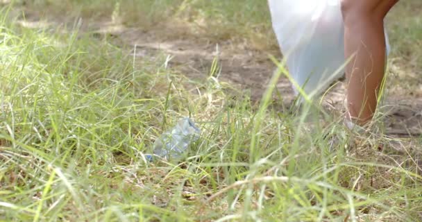 若い白人女性が草からペットボトルを拾い ゴミを集めている 彼女は時計を身に着けていて 昼間は屋外の清掃活動に従事しています — ストック動画