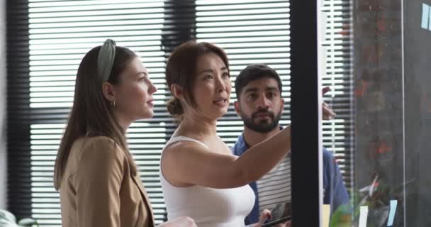 身穿米色西装的亚洲女商人正在向一位年轻的白人妇女展示一块玻璃板 两人似乎都在现代办公环境中进行着商业讨论 — 图库视频影像