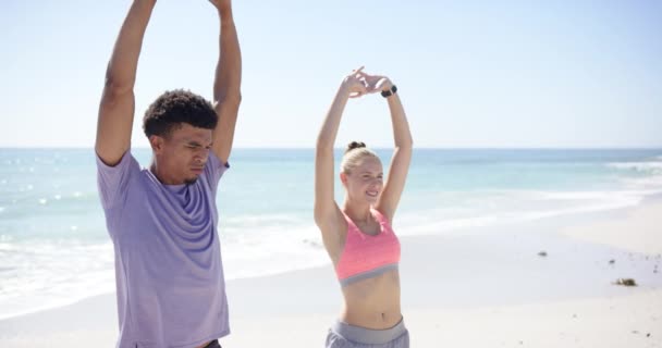 年轻的白人男子和白人女子伸展在阳光灿烂的海滩上 两人都穿着休闲运动服 在海空相映 动作缓慢的背景下 提倡健康的生活方式 — 图库视频影像