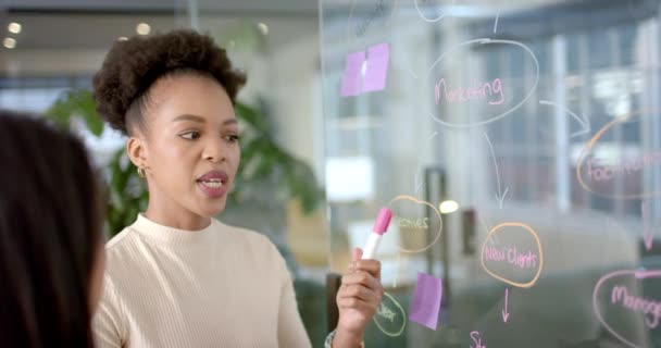 若いアフリカ系アメリカ人女性がオフィスでビジネスマーケティング戦略を発表 彼女は透明なアイデアボード上の同僚と関わり コラボレーション スローモーションを強調しています — ストック動画