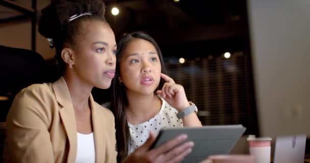 年轻的非洲裔美国妇女和生小孩的妇女在一个商业办公室里合作 他们专注于数字平板电脑 讨论一个项目或策略 慢动作 — 图库视频影像