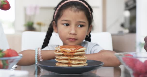 Biracialの女の子は シロップとフルーツで彼女を助ける手として朝食を楽しんでいます 彼女は家にいて 家族のケアと栄養 ゆっくりとした動きに焦点を当てて パンケーキのスタックに喜んでいます — ストック動画