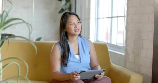 Mulher Biracial Senta Confortavelmente Sofá Amarelo Segurando Tablet Ela Aparece — Vídeo de Stock