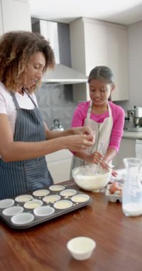 Çift ırklı mutlu anne ve kızın kek pişirdiği, mutfakta kek yaptığı dikey video, yavaş çekim. Yemek, yemek pişirme, annelik, çocukluk, birliktelik, ev hayatı ve yaşam tarzı, değişmemiş.