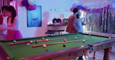 Çeşitli arkadaşlar odaya doğum günü afişi altında giriyor, selfie çekiyor, bilardo oynuyor ve dans ediyorlar. Parti, kutlama, gece hayatı, eğlence, canlı, sosyalleşme, eğlence