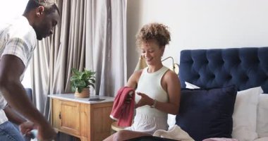 Çeşitli çiftler yataktaki açık bavullarına bitki ve akıllı telefonlarıyla kıyafet dolduruyorlar. Seyahat, organizasyon, yaşam tarzı, konfor, samimiyet, hazırlık, yerli