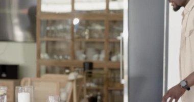 Adam, evde çeşitli aile yemekleri için çiçek ve bardaklarla yemek masası hazırlıyor. Hazırlık, sofra kurma, misafirperverlik.