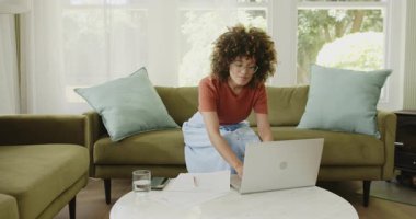 Evde bilgisayarlı ve akıllı telefonlu belgeleri inceleyen bir kadın. Uzaktan çalışma, ev ofisi, teknoloji, iş, çoklu görev, üretkenlik