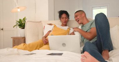 Yatakta dinlenen, dizüstü bilgisayar izleyen ve evde gülümseyen bir çift. Yaşam tarzı, eğlence, eğlence, teknoloji, mutluluk, bağ.