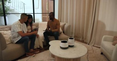 Çeşitli çiftler modern oturma odasındaki koltukta danışmanla ev tasarımı fikirlerini tartışıyor. İç mekan, yaşam tarzı, danışmanlık, işbirliği, beyin fırtınası, mimari