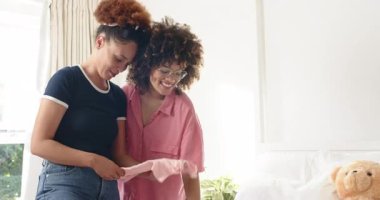 Lezbiyen çift çamaşırları yatağın üzerine katlıyor, evde oyuncak ayıyla kıyafet düzenliyorlar. ev işleri, ev işleri, birliktelik, ilişki, aile, derleme