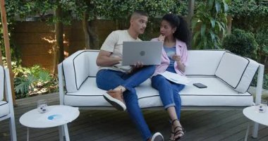 Çeşitli çiftler bahçe kanepesinde dizüstü bilgisayar kullanarak bahçede birlikte vakit geçiriyorlar. Teknoloji, eğlence, rahatlama, kablosuz, iletişim, bağ.