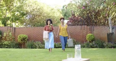 Lezbiyen çift güneşli arka bahçedeki çimlere piknik battaniyesi seriyorlar. Arka bahçede, rahatlık, rahatlama, bahar, yaşam tarzı, doğa.