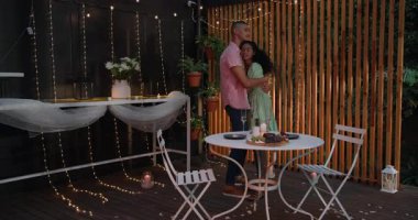 Farklı çiftler, peri ışıkları ve mum ışığında akşam yemeği eşliğinde romantik avluda kucaklaşıyorlar. Aşk, akşam, mum ışığı, yemek, yakınlık, açık hava.