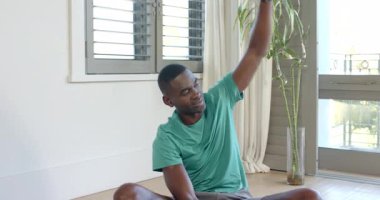 Evde, yoga minderinin üzerinde bambu saplarıyla bacak bacak bacak üstüne atmış oturan Afrikalı Amerikalı bir adam. Fitness, sağlık, meditasyon, farkındalık, minimalist, modern, iç mekan