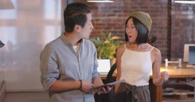 Asyalı meslektaşlar modern ofiste projeyi tabletlerle tartışıyor, birlikte gülümsüyorlar. Takım çalışması, işbirliği, beyin fırtınası, teknoloji, dijital, iş toplantısı