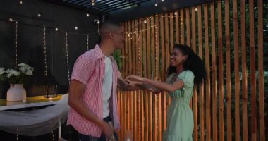 Çeşitli çiftler mum ışığında akşam yemeği ve ip ışıklarıyla romantik bir avluda kucaklaşıyorlar. Aşk, mum ışığı, samimiyet, akşam, ortam.