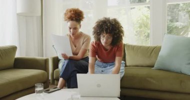 Çift cinsiyetli lezbiyen çift evdeki bilgisayarlarıyla birlikte kanepede belgeleri gözden geçiriyorlar. LGBTQ, ortaklık, evrak işleri, ev ofisi, takım çalışması, ilişki