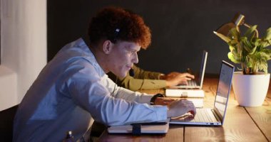 Ofiste geç saatlere kadar çalışıyor, çeşitli profesyoneller dizüstü bilgisayar ve kulaklık kullanıyor, görevlere odaklanıyor. İş, takım çalışması, teknoloji, işbirliği, üretkenlik, kurumsal