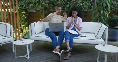 Çeşitli çiftler bahçede dizüstü bilgisayar ve akıllı telefon kullanırken belgeleri tartışıyorlar. İş, takım çalışması, işbirliği, teknoloji, iletişim, yaşam tarzı