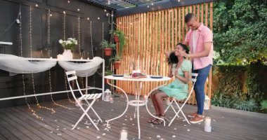 Verandada romantik bir akşam yemeği. Çiçekler ve ışıklarla mum ışığında eğlenen farklı bir çift. Aşk, randevu gecesi, yemek, mum ışığı, bahçede.